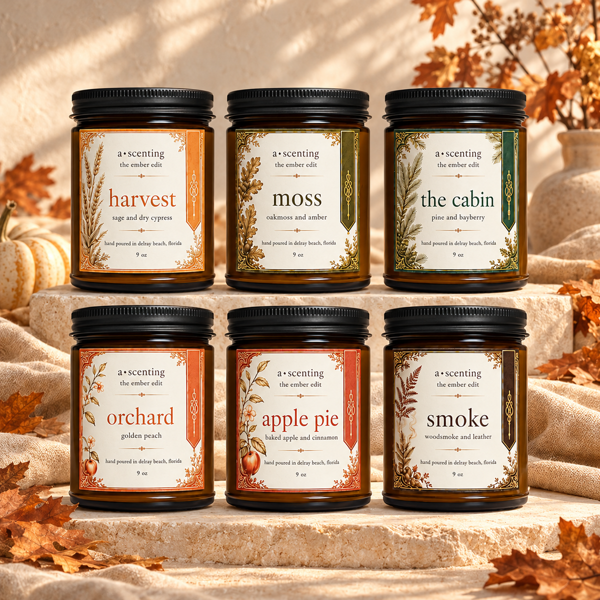Six 9 oz Ember Edit amber jar candles on cream stone with linen, autumn leaves and warm golden light: Harvest, Moss, The Cabin, Orchard, Apple Pie and Smoke.